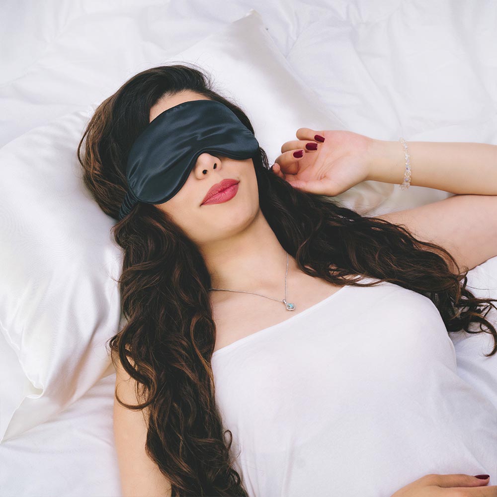 En tjej ligger med en svart siden sovmask på